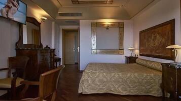 A hotel room with a large bed, wooden furniture, a television, and artwork on the walls.