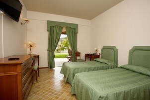 A hotel room with two beds, a desk, a chair, a TV, and a window with curtains.