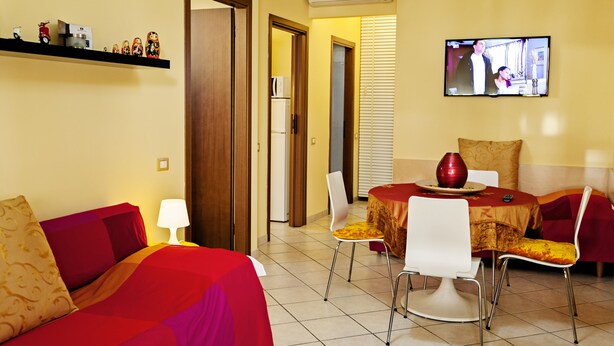 A living room with a sofa, a dining table with chairs, a TV mounted on the wall, and a door leading to another room. - Bed & Breakfast Ai Cipressi (Lucca)