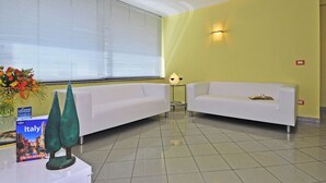 Una zona de recepción con dos sofás blancos, una mesita con un florero y una lámpara, además de un libro.