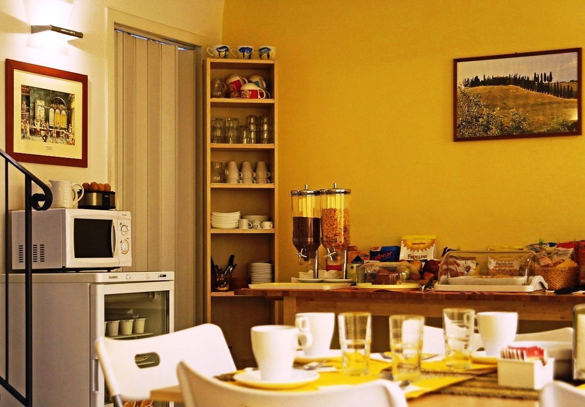 A dining area with a table set for two, a microwave, a refrigerator, and shelves with dishes and condiments.