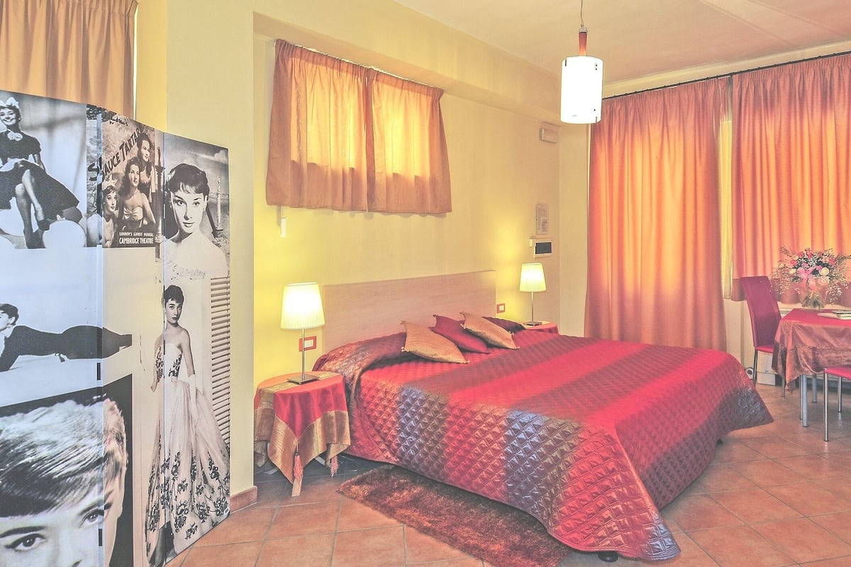 Une chambre d’hôtel avec un lit, deux tables de chevet avec des lampes, un téléviseur fixé au mur et une affiche accrochée au mur.