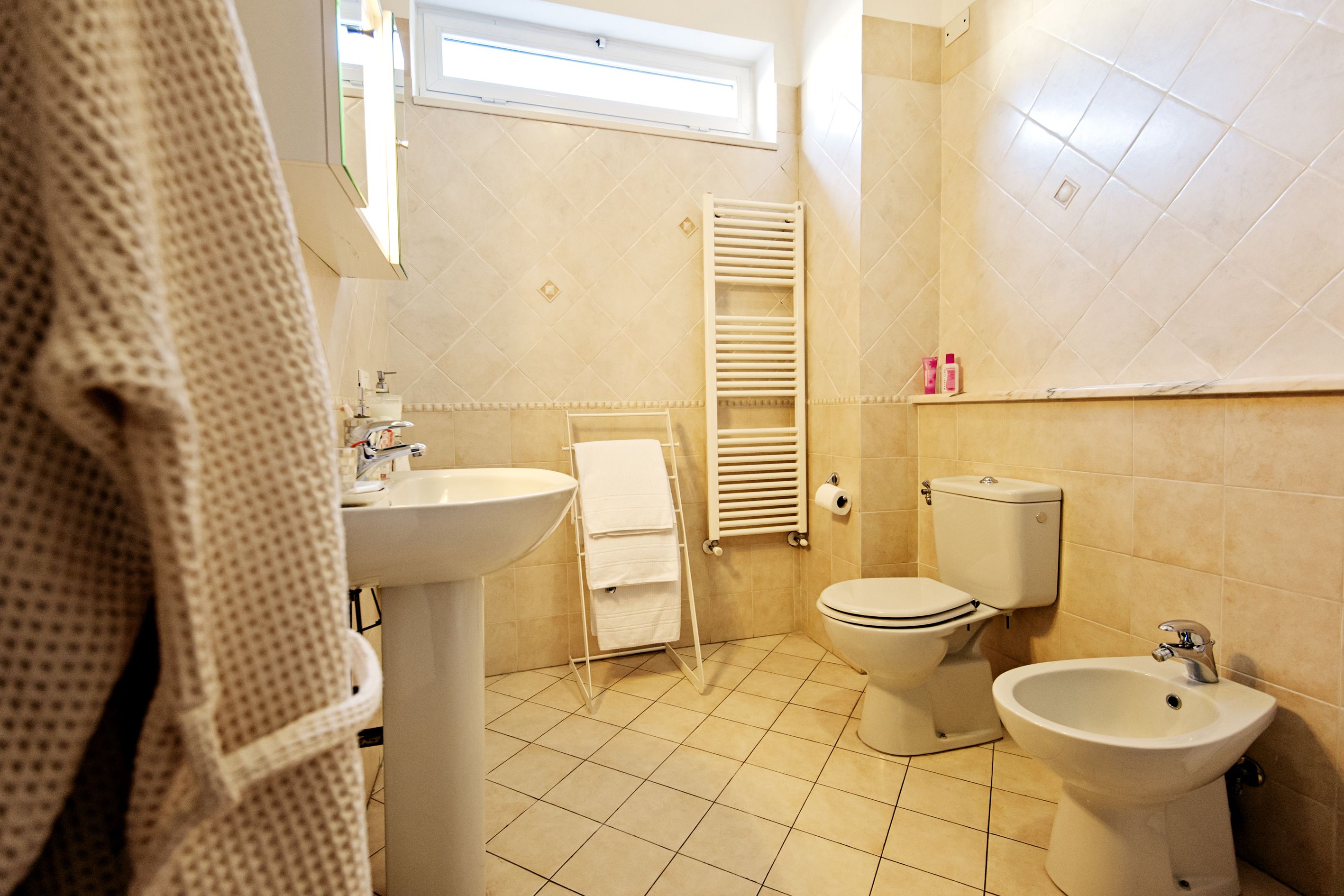 A bathroom with a sink, toilet, bidet, and towel rack.