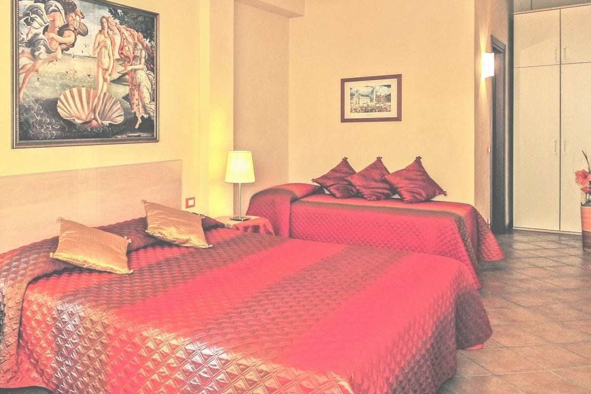 Une chambre d’hôtel avec deux lits, un tableau au mur et une photographie encadrée au-dessus du lit.