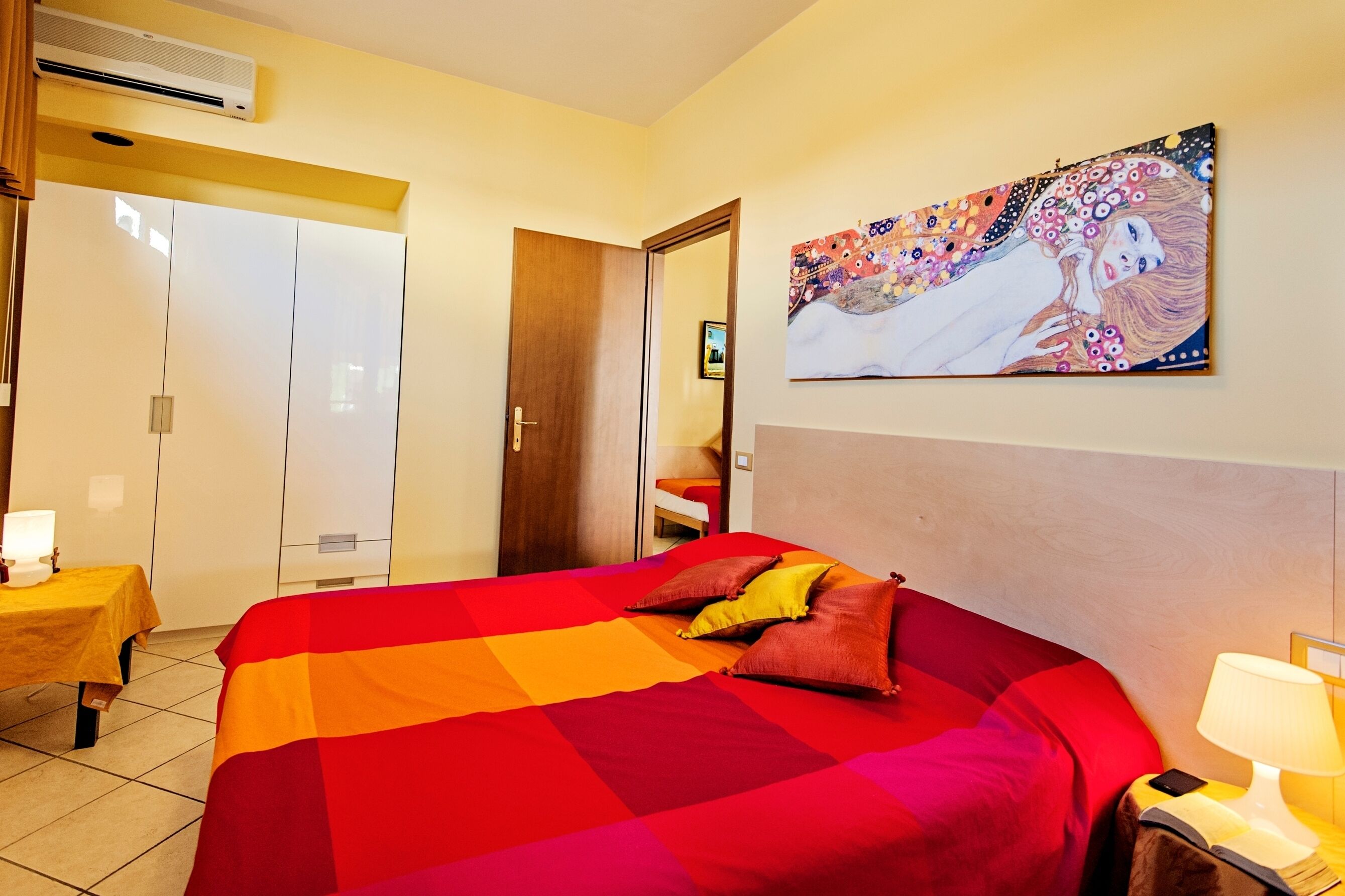 Une chambre d’hôtel avec un grand lit, une table de chevet avec une lampe, un tableau au mur et une armoire.