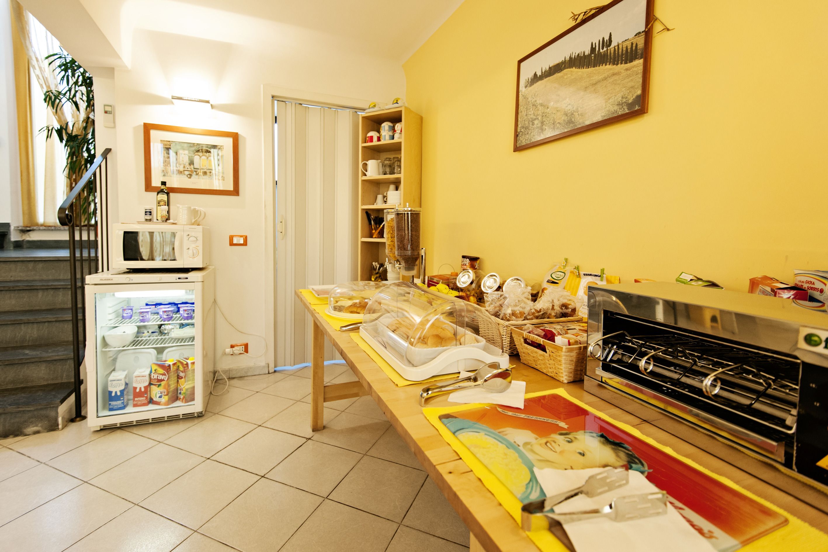 A kitchen with a microwave, refrigerator, and a stove. There is a table with food items and a painting on the wall.