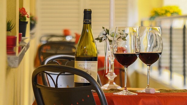 Una mesa dispuesta con una botella de vino, dos copas de vino, una vela encendida y una silla.