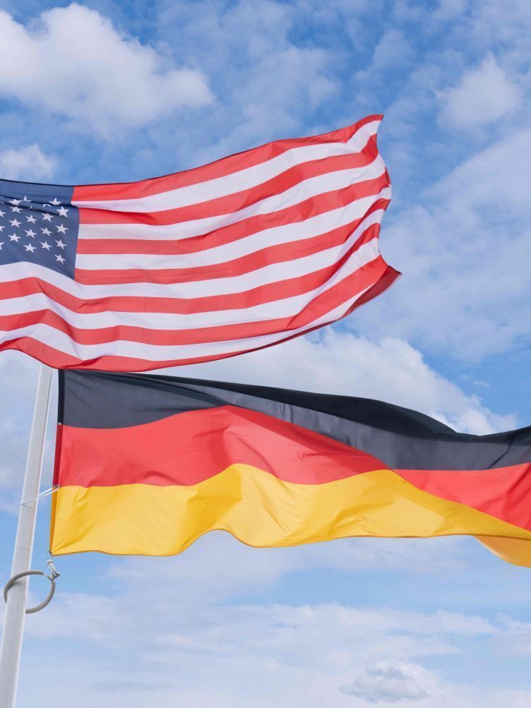 Due bandiere, una degli Stati Uniti e una della Germania, issate su un'asta con cielo sereno sullo sfondo.