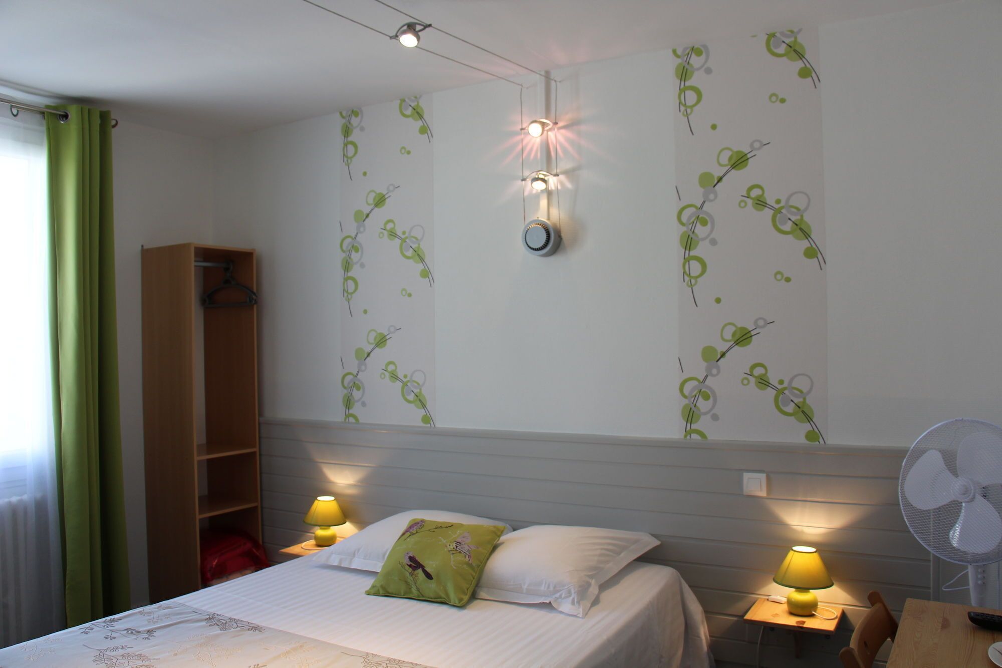 A bedroom with a bed, two bedside lamps, a wall-mounted light fixture, a ceiling fan, and a green curtain.