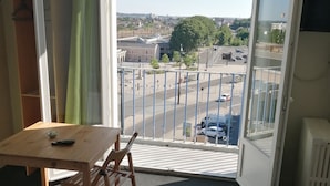 A room with a bed, a table, and a chair. There is a balcony with a view of the street and buildings. - Hotel d Orléans (Angouleme)