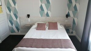 A hotel room with a bed, two pillows, a bedside table, a wall clock, and geometric patterned wallpaper. - Hotel d Orléans (Angouleme)
