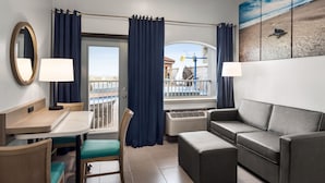 A hotel room with a balcony, a dining area, a sofa, and a painting of a beach scene. - La Copa Inn Beach Hotel (South Padre Island)