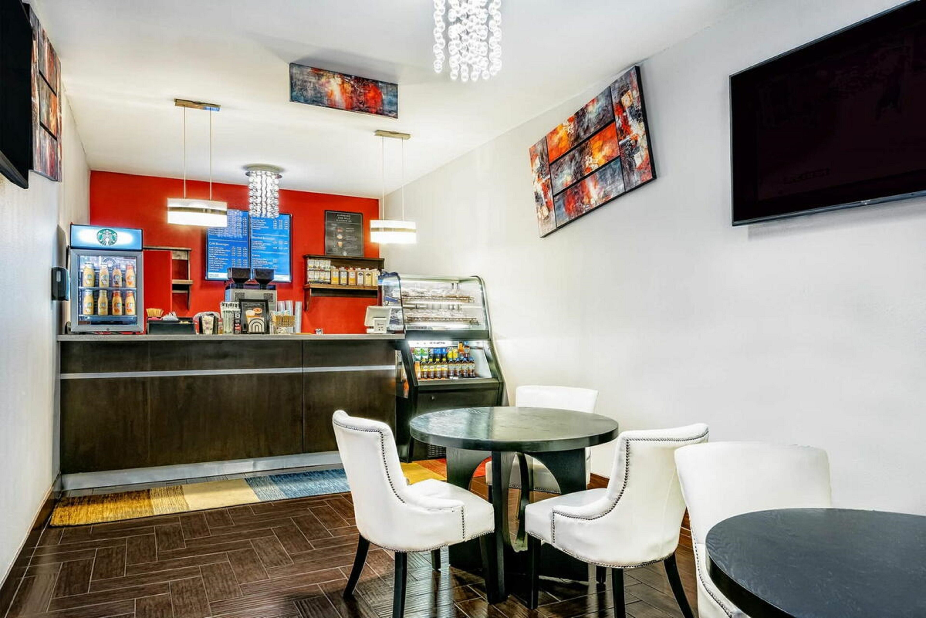 A modern restaurant with a red accent wall, a bar area, and a seating arrangement with white chairs and a round table.