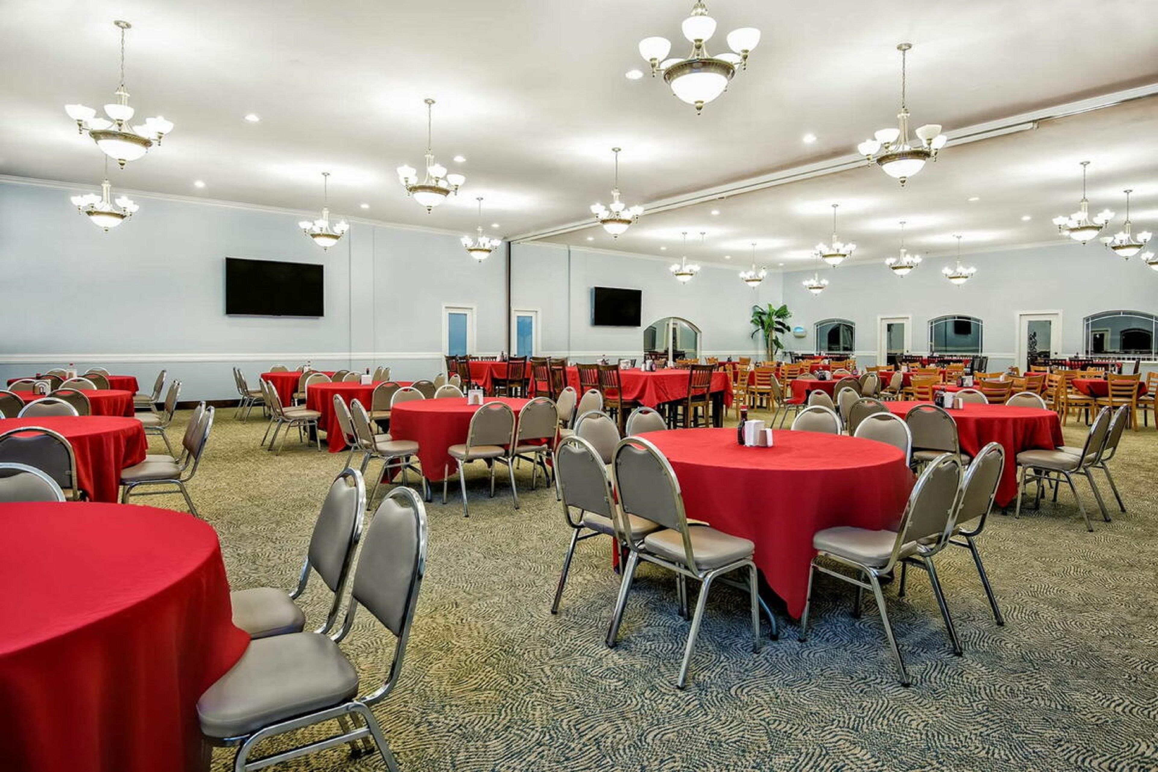 A banquet hall with round tables covered in red tablecloths, arranged in rows.