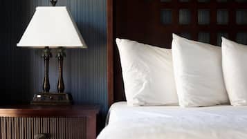 A neatly made bed with white linens and pillows, a wooden nightstand with a lamp, and a dark wooden headboard.