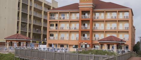 A multi-story hotel with balconies, a covered walkway, and a beach view.
