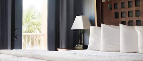 Habitación de hotel con una cama grande, una mesita de noche con lámpara y vistas a palmeras a través de una puerta corrediza.