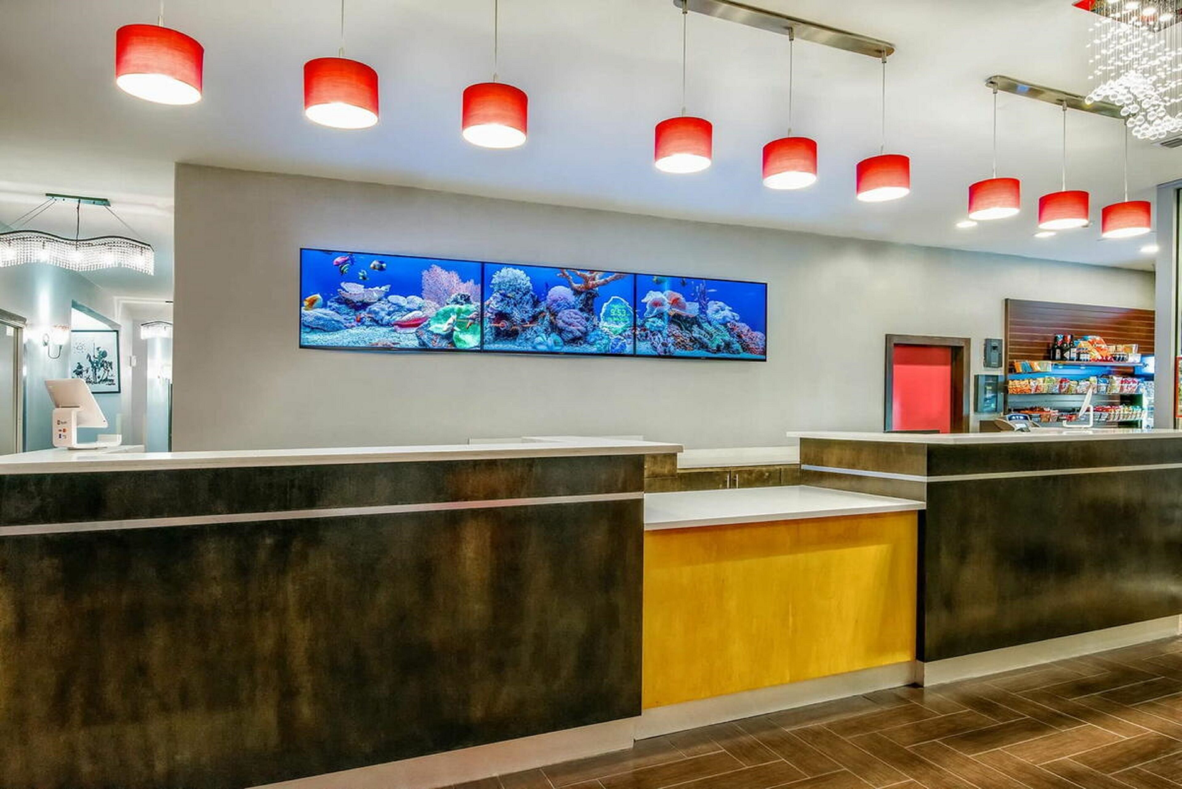 A reception area with a large aquarium display, a counter with a digital screen, and red pendant lighting.