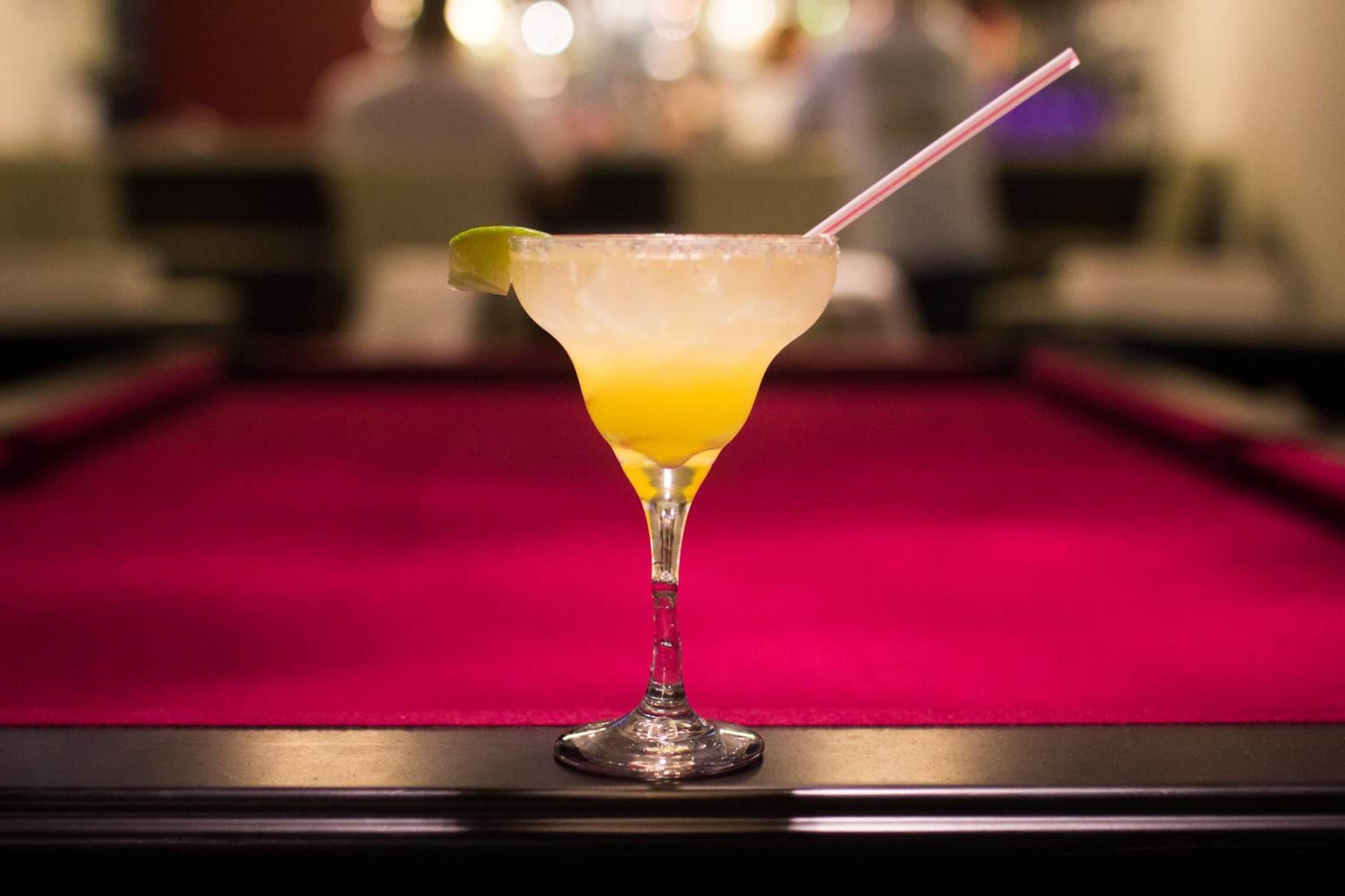 Een cocktail in een martini glas met een limoenpartje op een pooltafel.