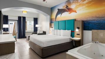 Une chambre d’hôtel moderne dotée d’un grand lit, d’un coin salon, d’un bureau, d’une salle de bain avec baignoire et d’une fresque représentant des dauphins sur le mur.