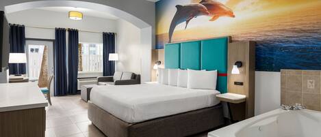 Una habitación de hotel moderna con una cama grande, zona de estar, escritorio, baño con bañera y un mural de delfines en la pared.