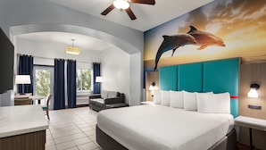 A hotel room with a large bed, a desk, a chair, a sofa, and a mural of dolphins on the wall. - La Copa Inn Beach Hotel (South Padre Island)