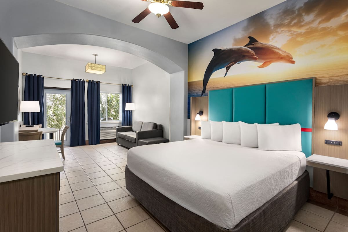 Habitación de hotel con una cama grande, un escritorio, una silla, un sofá y un mural de delfines en la pared.