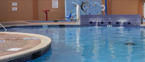 Una piscina con un mural de delfines, un elemento acuático y un puesto de salvavidas.