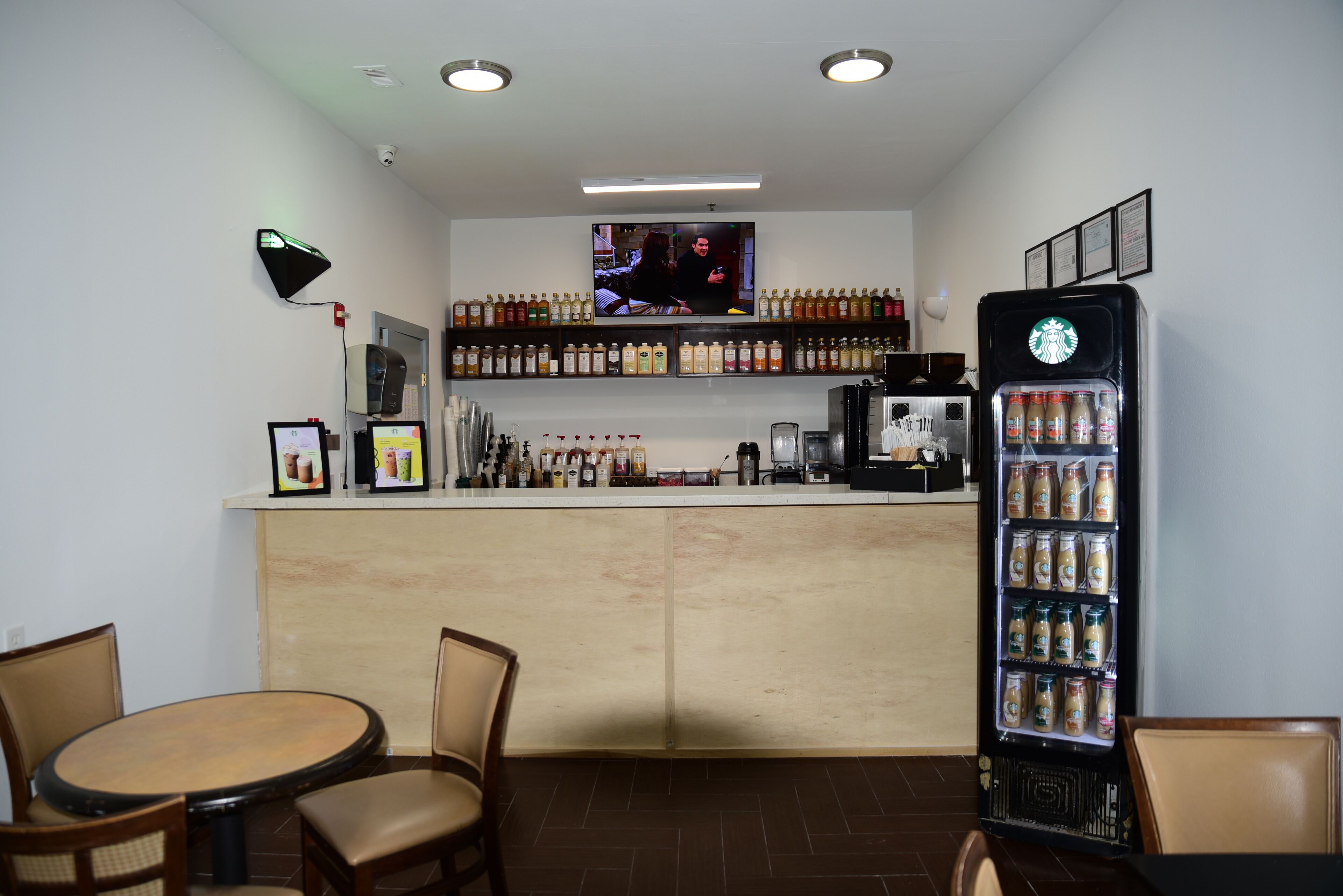 A bar area with a TV, shelves of beverages, a coffee machine, and seating.