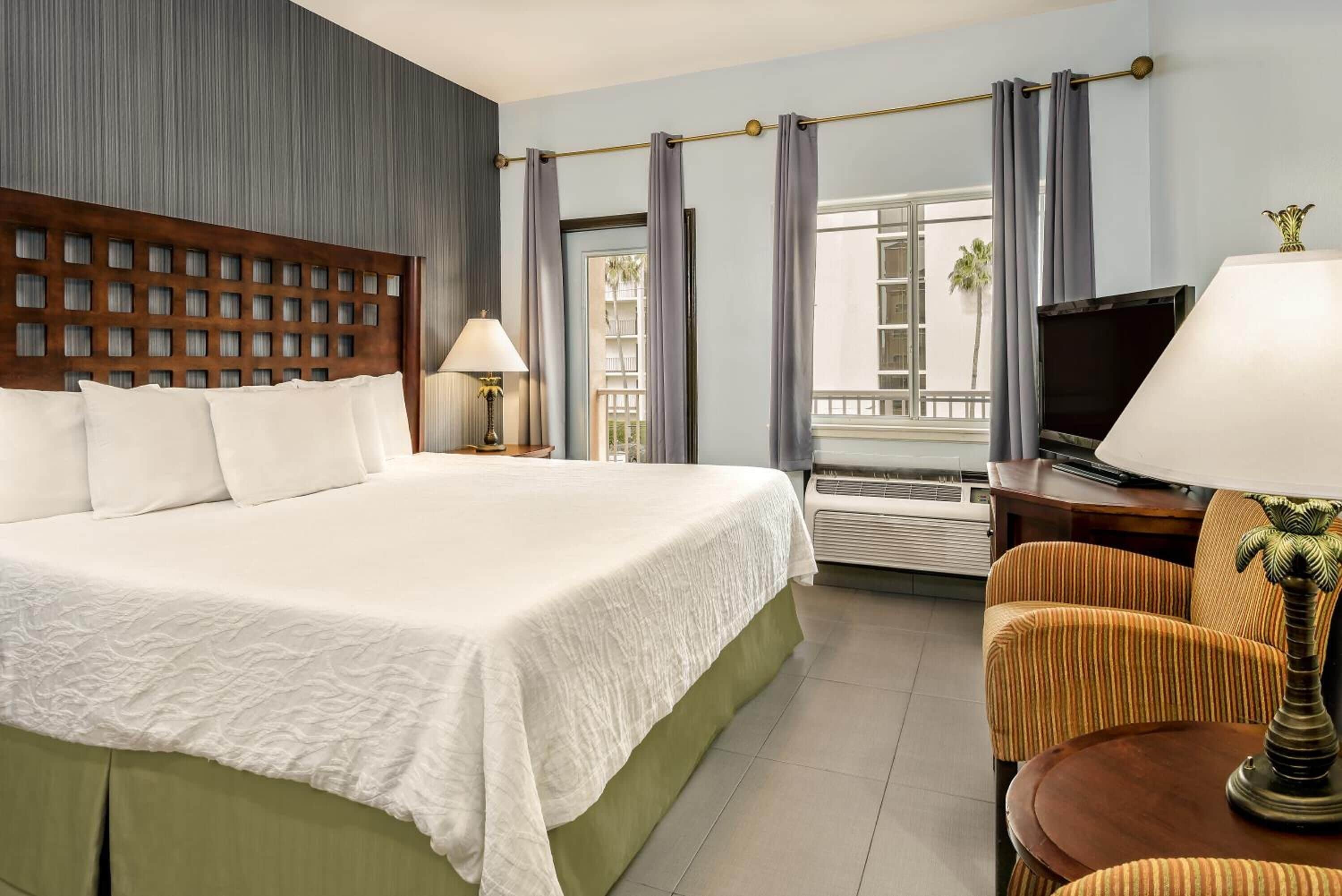 A hotel room with a large bed, a television, a chair, and a window with curtains.