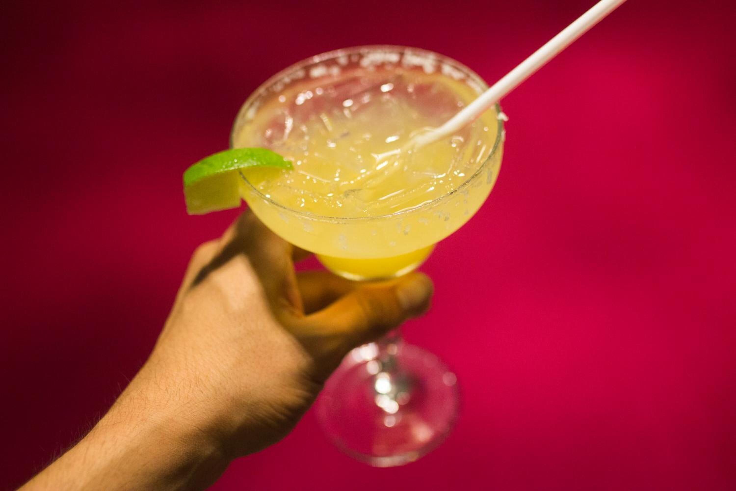 A hand holding a cocktail glass with a lime wedge and a straw.
