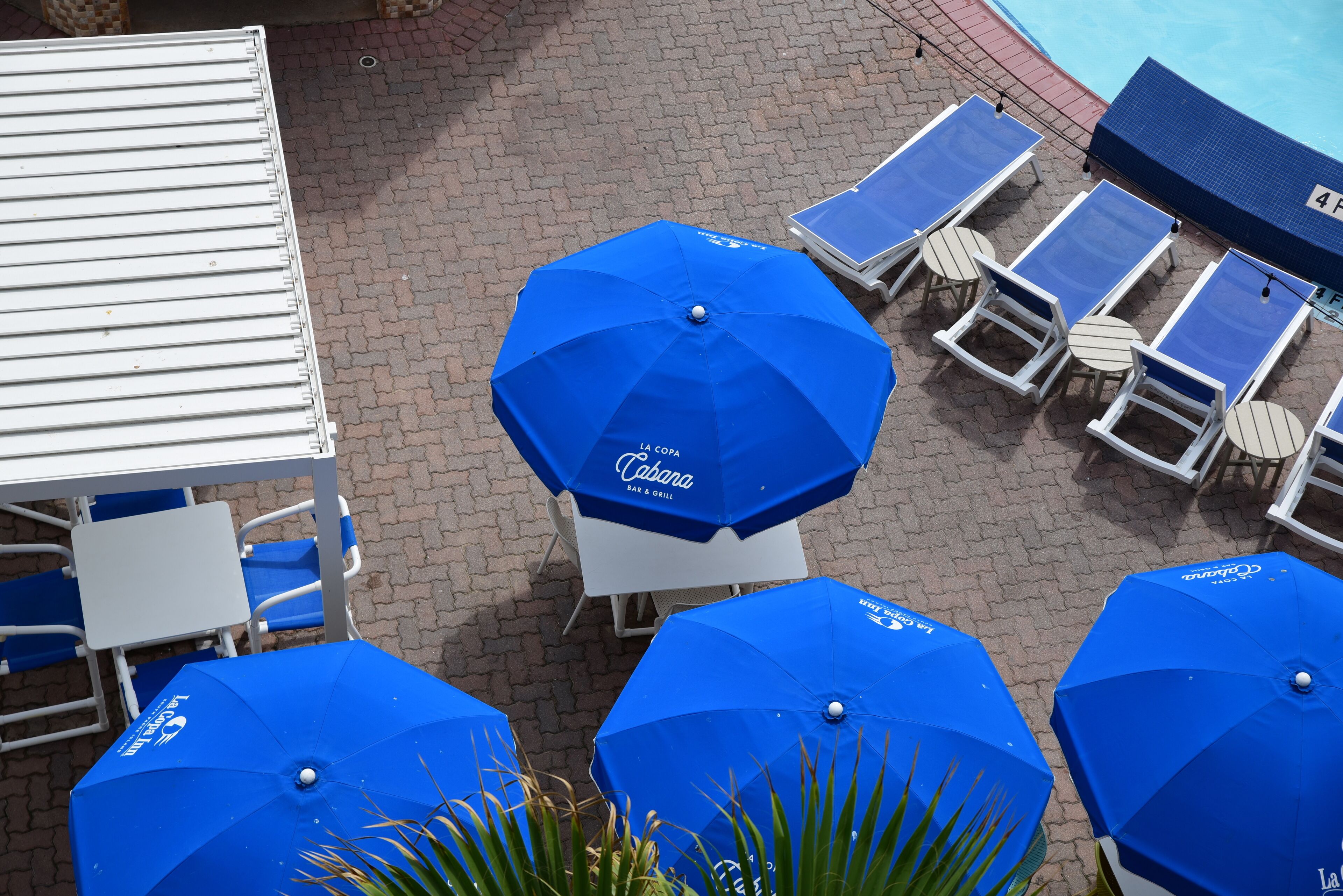A poolside area with blue umbrellas, lounge chairs, and a white table.