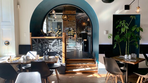 A restaurant interior with a wooden table and chairs, a staircase leading to the kitchen, and a large plant on the right. - Hôtel Sainte-Anne (Québec City)