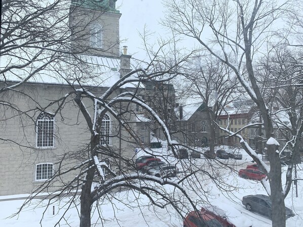 A snow-covered building with a clock tower, parked cars, and bare trees.