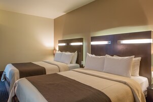 Una habitación de hotel con dos camas, cada una con cabecera y lámparas de noche.