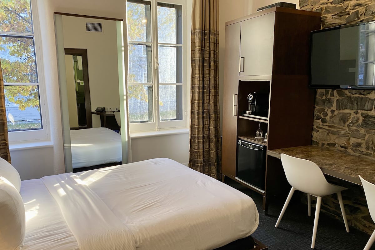 Une chambre d’hôtel avec un lit, un bureau, une télévision et un mur en pierre.