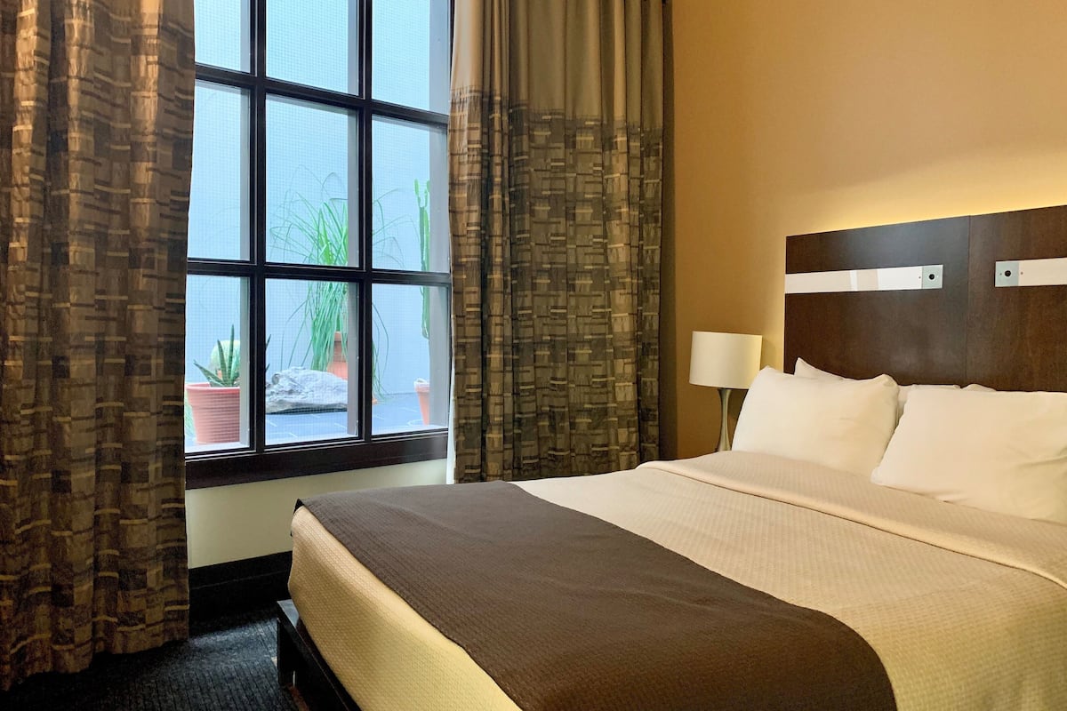 Une chambre d’hôtel avec un grand lit, une fenêtre avec des rideaux, une table de chevet avec une lampe et une vue sur l’extérieur.