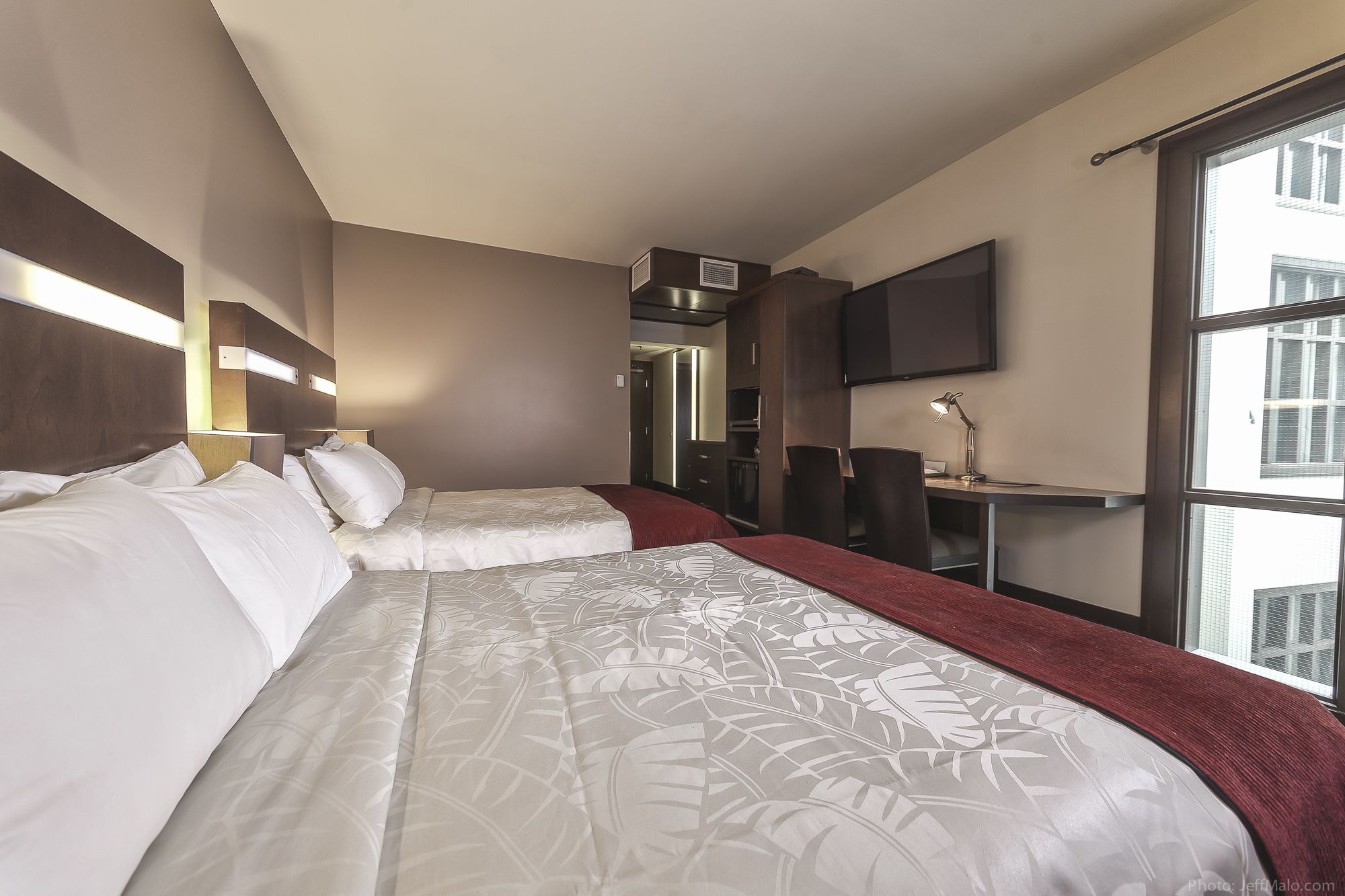 Une chambre d’hôtel avec deux lits, un bureau, une chaise, une télévision et une grande fenêtre.