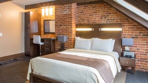 A hotel room with a brick wall, a bed with white linens, a desk with a lamp, and a small TV. - Hôtel Sainte-Anne (Québec City)