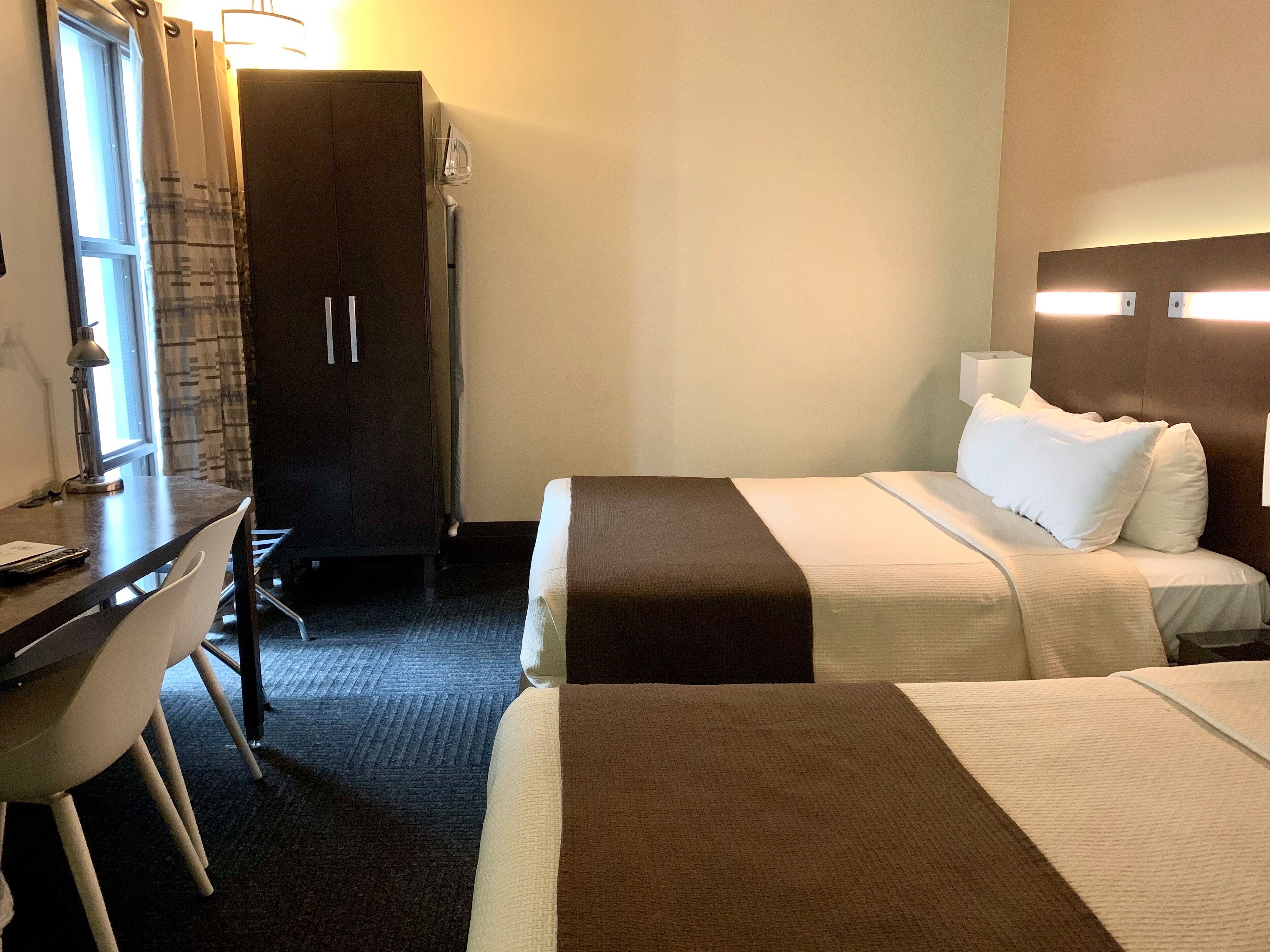 A hotel room with two beds, a desk, a wardrobe, and a window with curtains.