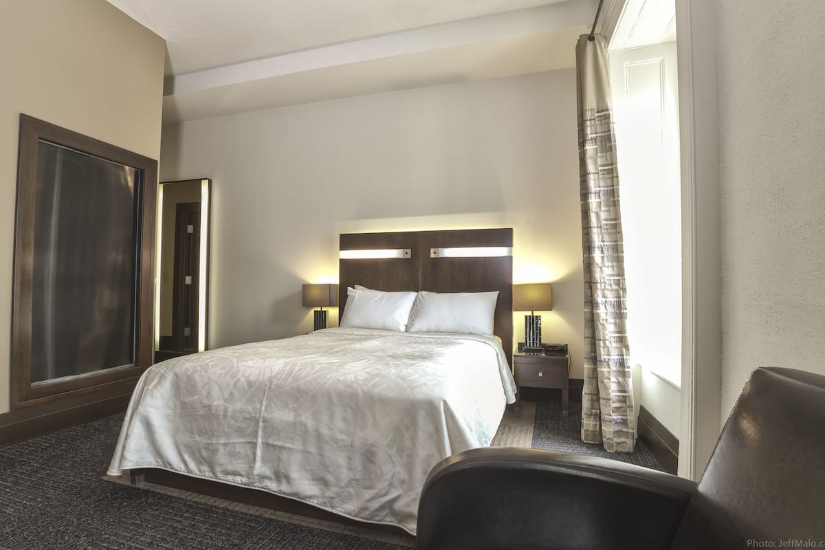 Une chambre d’hôtel avec un grand lit, deux lampes de chevet, une table de nuit, une chaise et une vue sur l’extérieur.