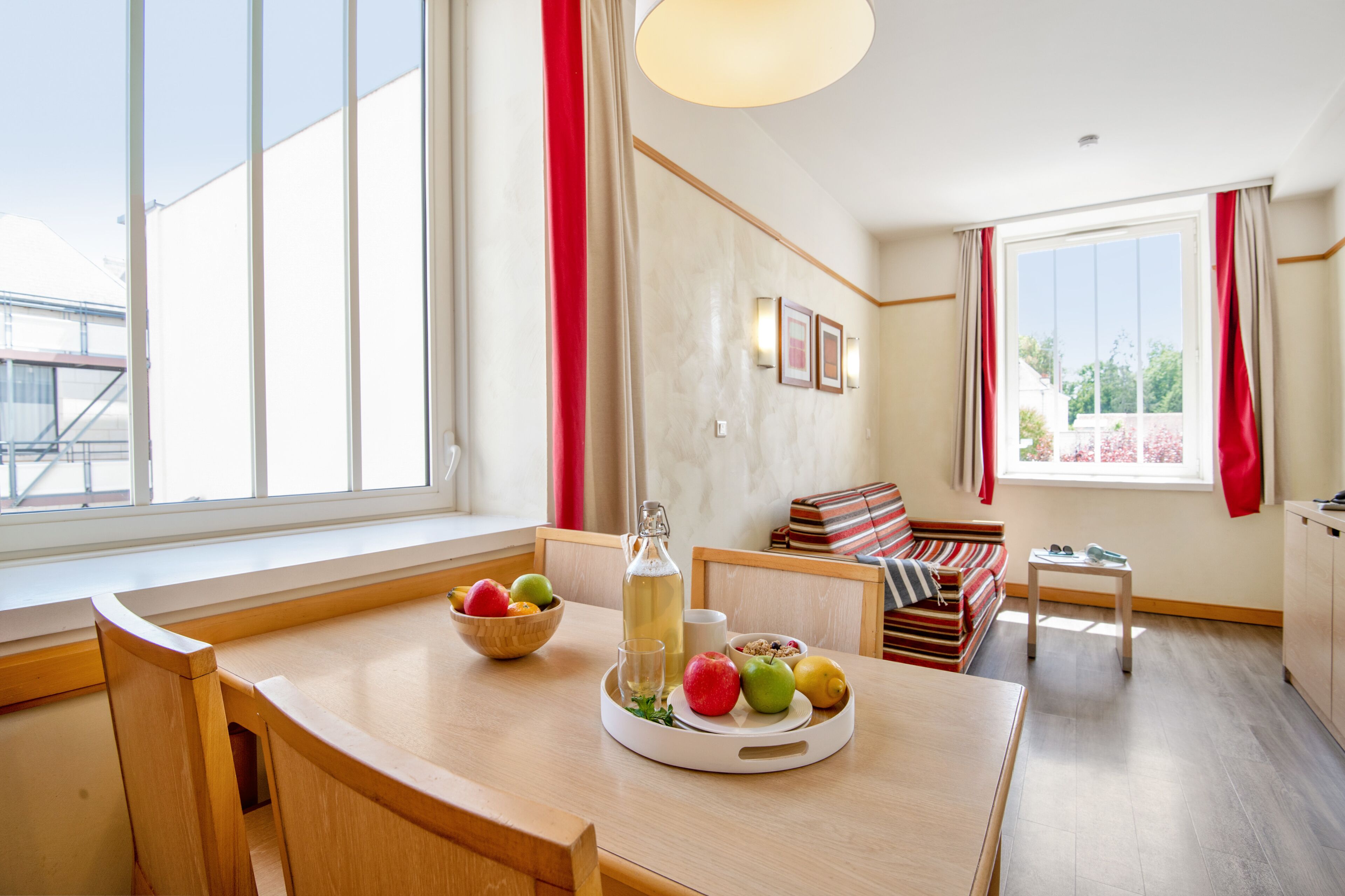Een moderne woonkamer met een houten eettafel, een bank en een raam met rode gordijnen.