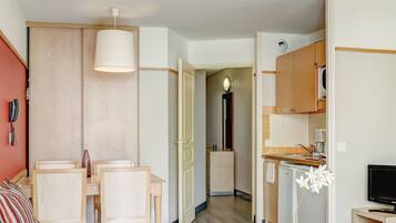 A compact living space with a sofa, dining table, kitchenette, and a TV.