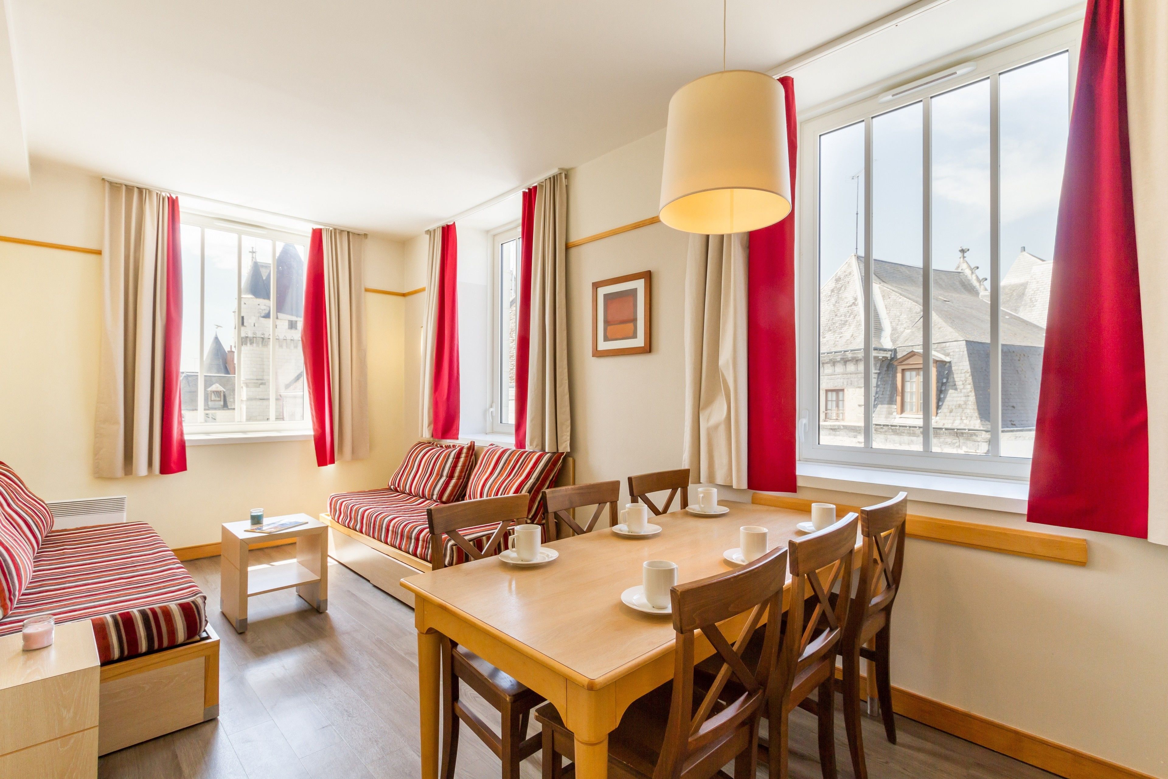 Une chambre d’hôtel comprenant un coin repas, un ensemble de canapés et une grande fenêtre avec des rideaux.