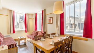 Une chambre d’hôtel comprenant un coin repas, un ensemble de canapés et une grande fenêtre avec des rideaux.