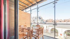 Un balcón con mesa y sillas de madera, ventanas amplias que dan a un edificio histórico.