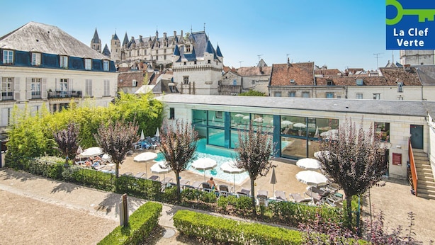 Un hotel con piscina, rodeado de sillones de descanso y sombrillas, con un castillo al fondo.