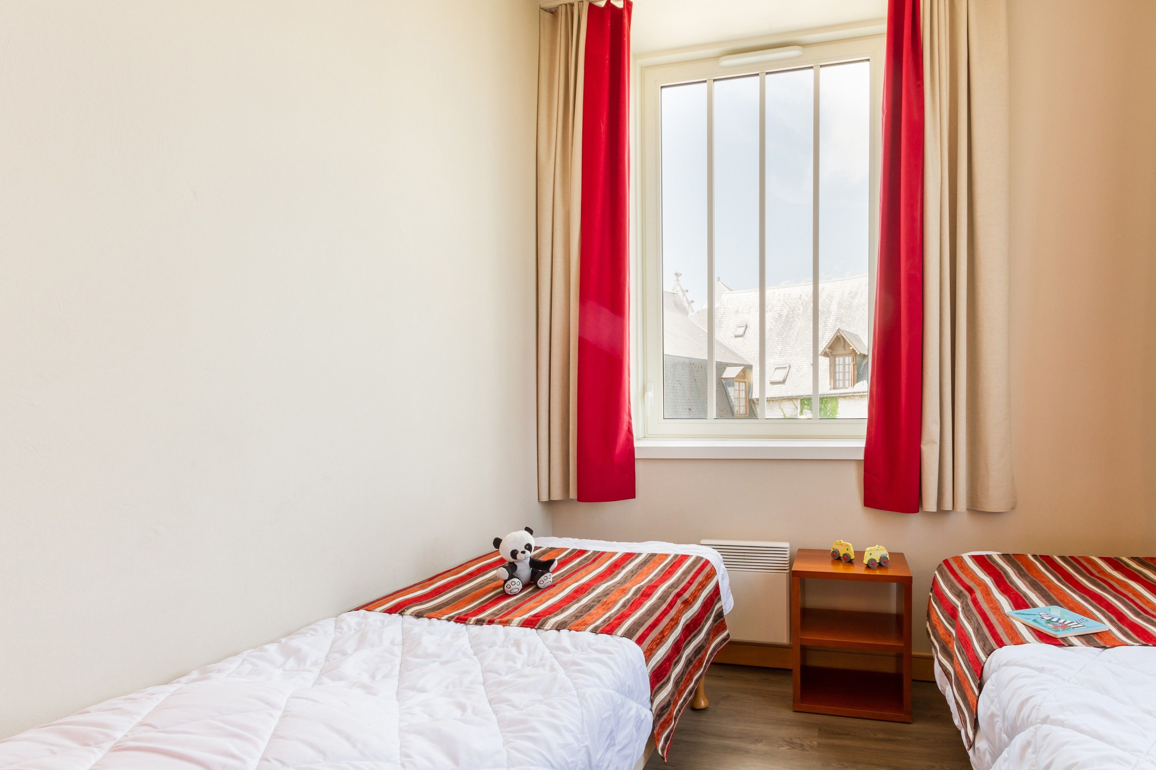 A room with two beds, a window with curtains, and a small table with toys.