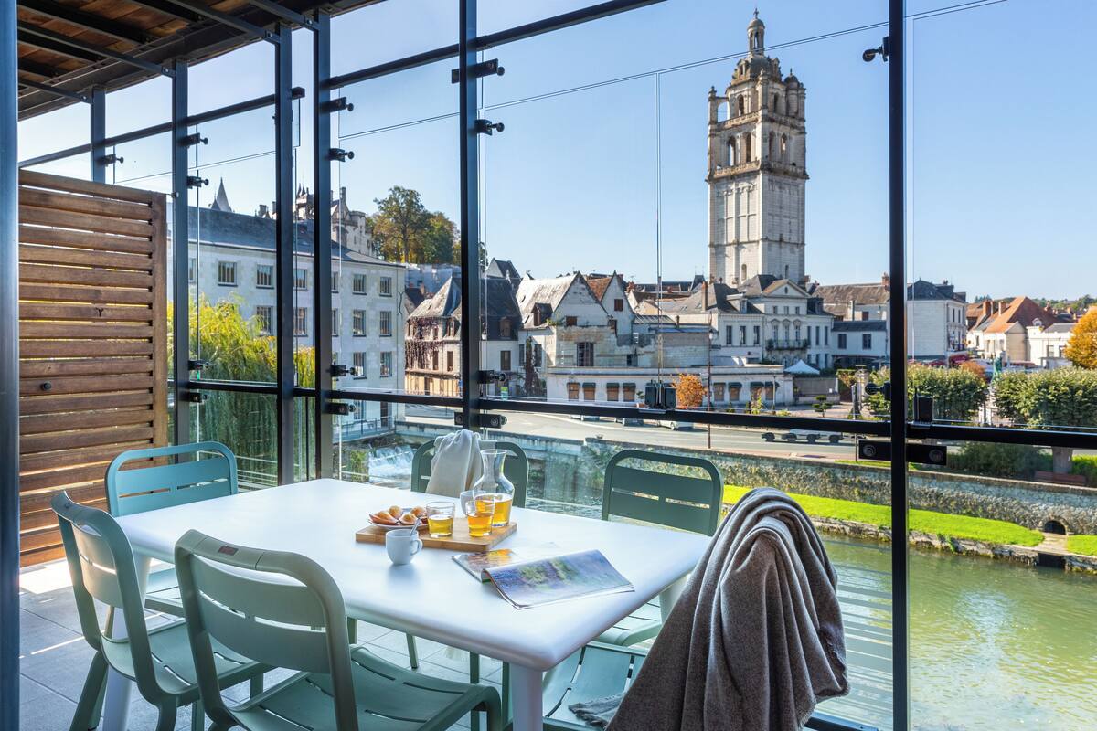 A table with chairs and a view of a historic tower through large windows.