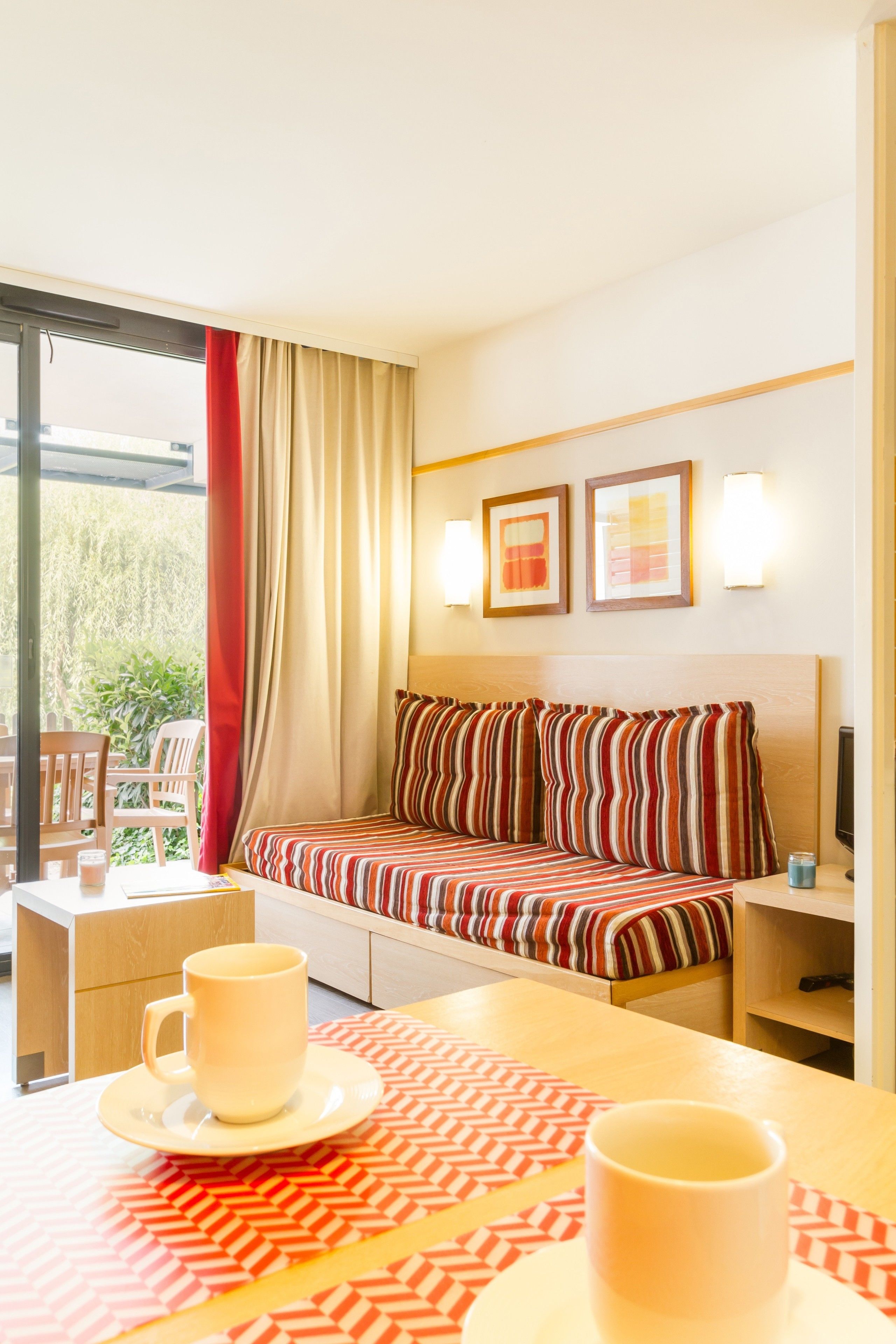 Quarto de hotel com uma cama, uma mesa com duas chávenas, uma cadeira e uma janela com cortinas.